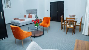 A hotel room with a bed, two orange chairs, a round table, and a dining set.