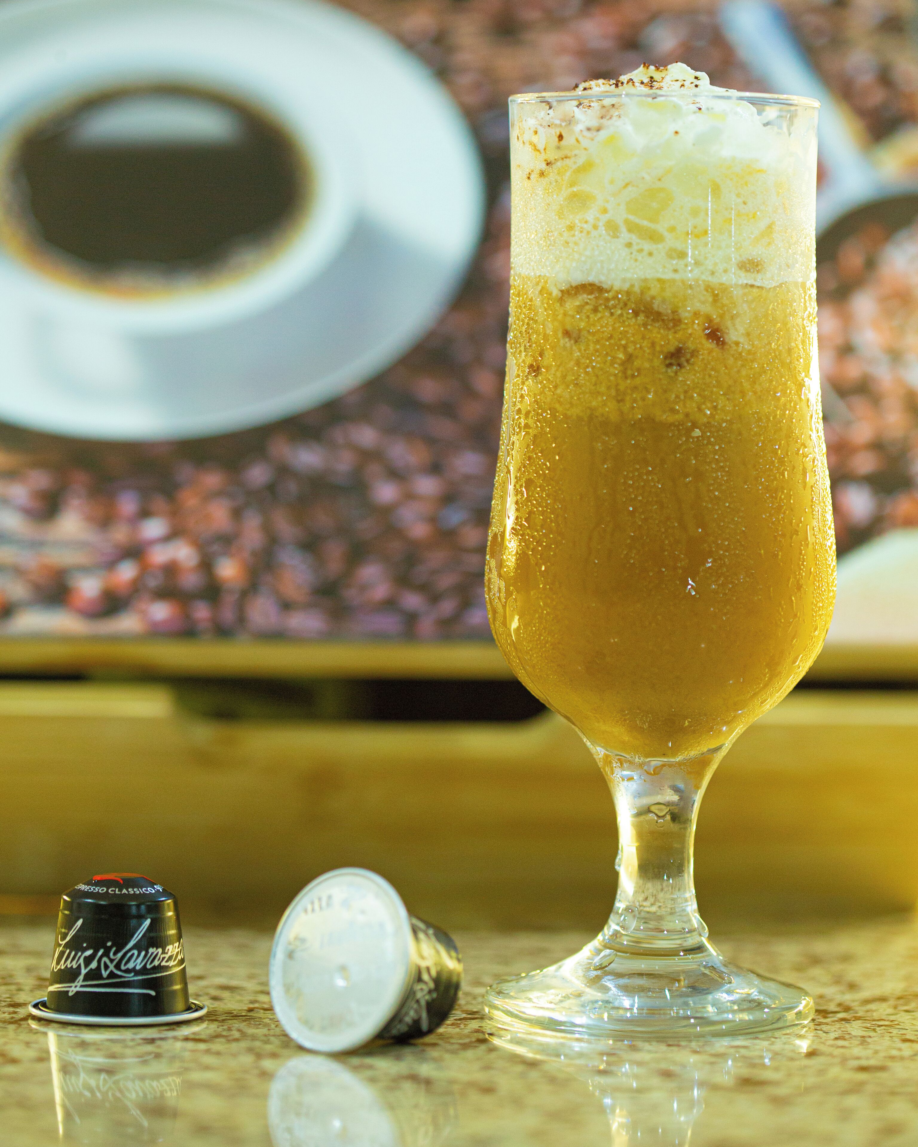 A tall glass of beer with foam on top, a bottle cap, and a bottle on a reflective surface.