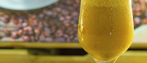 A tall glass of beer with foam on top, a bottle cap, and a bottle on a reflective surface.