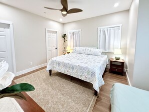A bedroom with a bed, a nightstand, a lamp, a ceiling fan, and a door. - "Hina Hideaway", Views, A/C, Walkable to Beach (Punaluu)