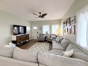 A living room with a sectional sofa, a television on a wooden cabinet, a ceiling fan, and a patterned rug. - "Hina Hideaway", Views, A/C, Walkable to Beach (Punaluu)