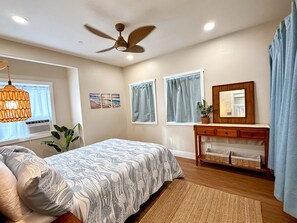 A bedroom with a bed, bedside table, curtains, a ceiling fan, and a window with blinds. - "Hina Hideaway", Views, A/C, Walkable to Beach (Punaluu)