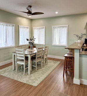 A dining area with a table, chairs, a ceiling fan, and windows with white curtains. - "Hina Hideaway", Views, A/C, Walkable to Beach (Punaluu)