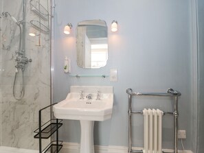 Ein Badezimmer mit einer Marmerdusche, einem weißen Waschbecken, einem Glastregal, einem Spiegel und einem Handtuchhalter.
