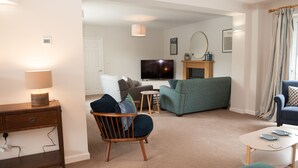 A modern living room with a sofa, armchair, TV, and a small table. - Brooklands (Lyme Regis)