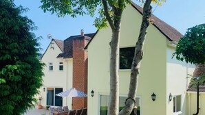 A two-story house with a patio area, a dining table with chairs, and a large umbrella. - Brooklands (Lyme Regis)