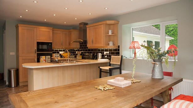 A modern kitchen with wooden cabinets, a central island, and a dining area with a wooden table and chairs. - Brooklands (Lyme Regis)