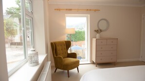 A bedroom with a large window, a wooden chair, a dresser, and a bed. - Brooklands (Lyme Regis)