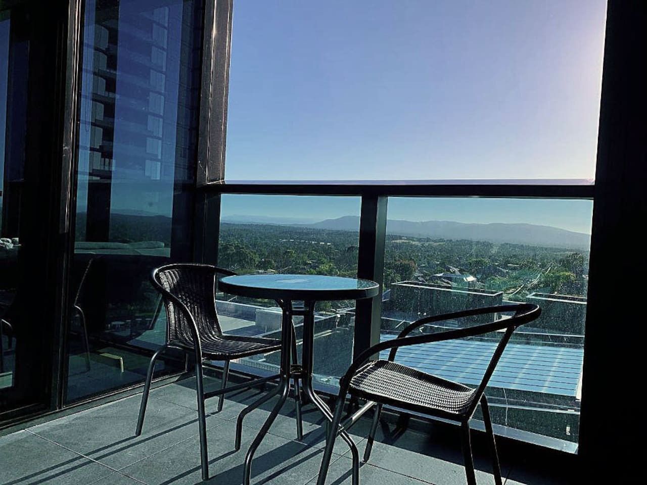 A balcony with two chairs and a table, overlooking a cityscape with buildings and a mountain in the distance.