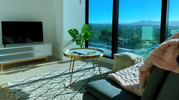 A modern living room with a flat-screen TV, a round coffee table, a potted plant, and a sofa with a blanket. - Skygarden Luxury 2-Bed, 2-Bath Apartment with Free Parking in Central Location (Glen Waverley)