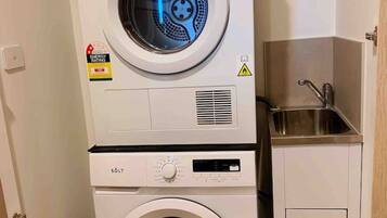 A stacked washer and dryer unit with a small sink and cabinet.