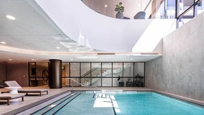 An indoor swimming pool with a modern design, including a curved ceiling and large windows. - Skygarden Luxury 2-Bed, 2-Bath Apartment with Free Parking in Central Location (Glen Waverley)