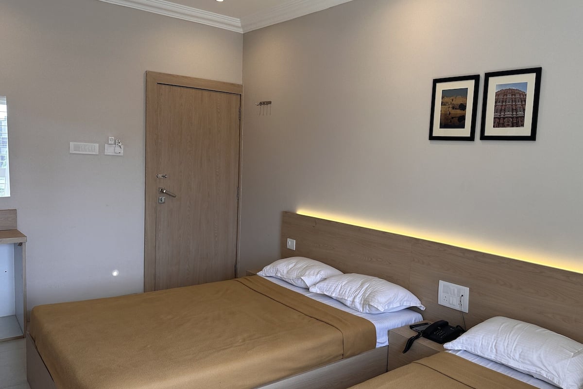 Una habitación de hotel con dos camas, una puerta de madera y dos cuadros en la pared.