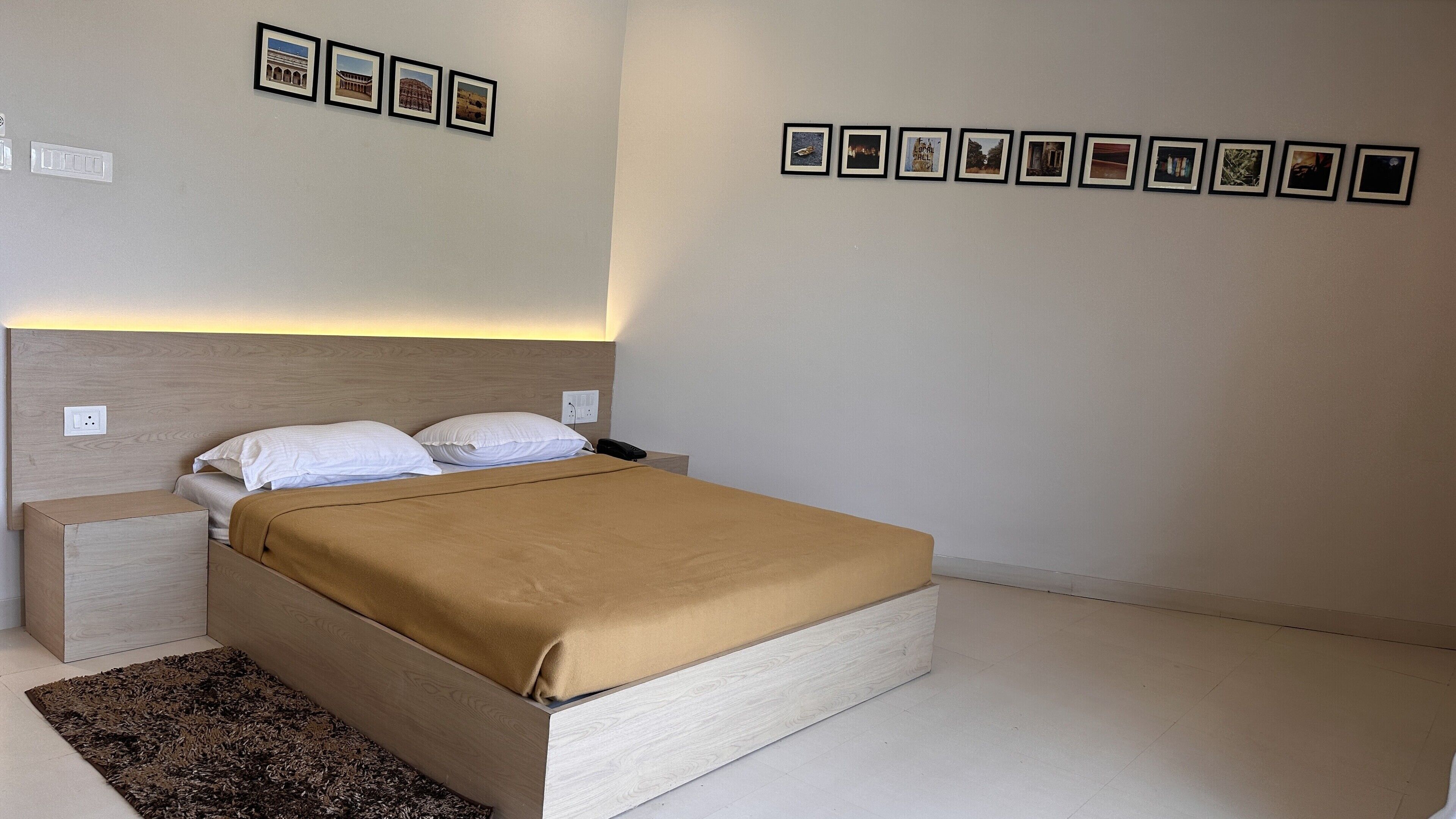 Een keurig opgemaakte slaapkamer met een bed, nachtkastjes en een aantal ingelijste foto’s aan de muur.