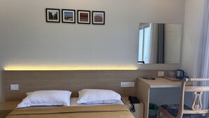 Une chambre d’hôtel avec un lit, deux oreillers, une table de chevet avec un téléphone, un miroir et trois tableaux encadrés accrochés au mur.