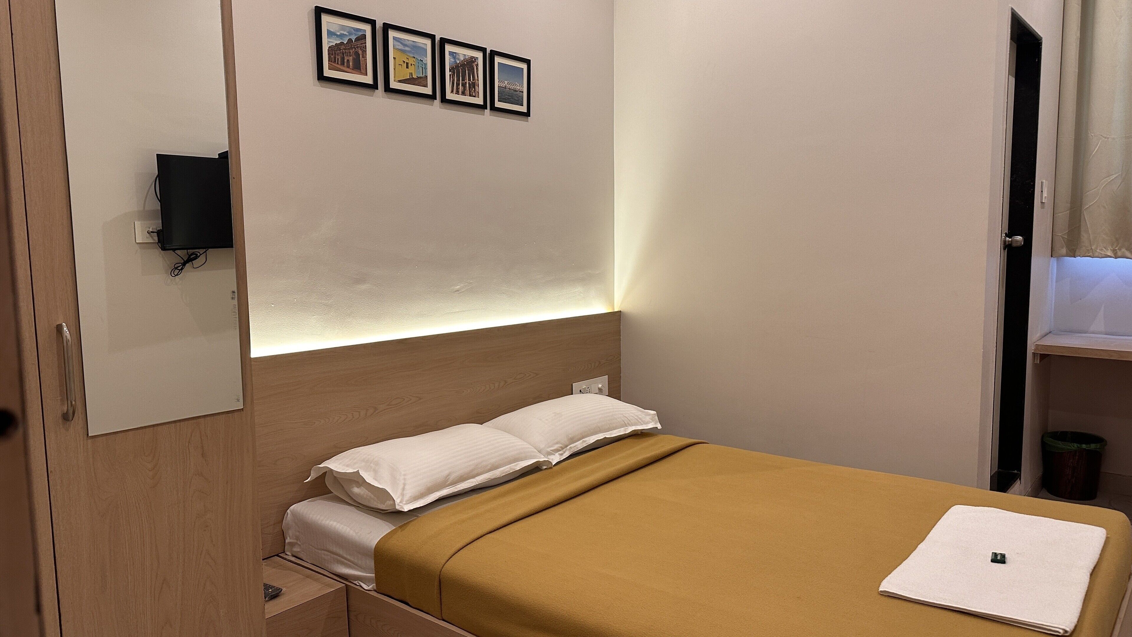 A bedroom with a bed, a bedside table, a wall-mounted TV, and a door.