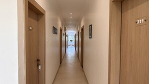 Un couloir d’hôtel avec des portes en bois, des panneaux indiquant le numéro des chambres et des tableaux encadrés accrochés aux murs.
