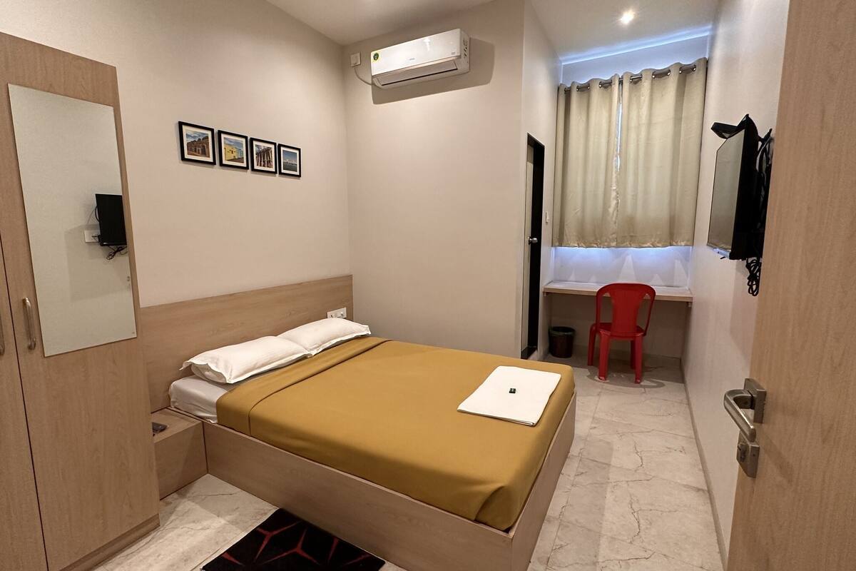 Un dormitorio con cama, escritorio, silla, aire acondicionado y ventana con cortinas.