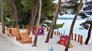 Une zone de plage avec des chaises longues en bois, une aire de jeux et un panneau indiquant la zone réservée à la baignade.
