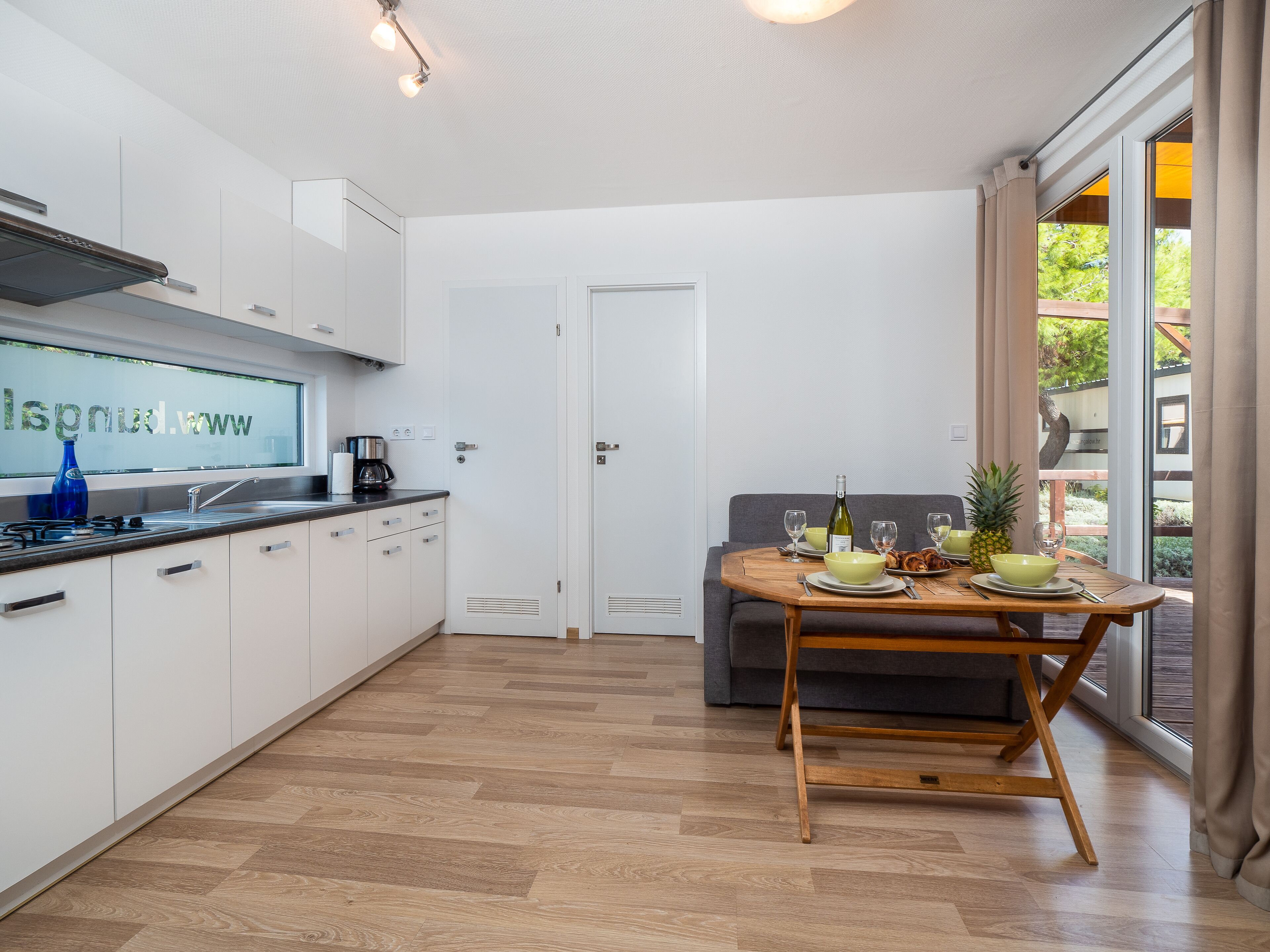 A modern kitchen with white cabinets, a built-in stove, and a window with a view of greenery.