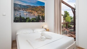 Une chambre d’hôtel avec un lit, une table de chevet, une fenêtre avec des rideaux et un tableau représentant une ville côtière.