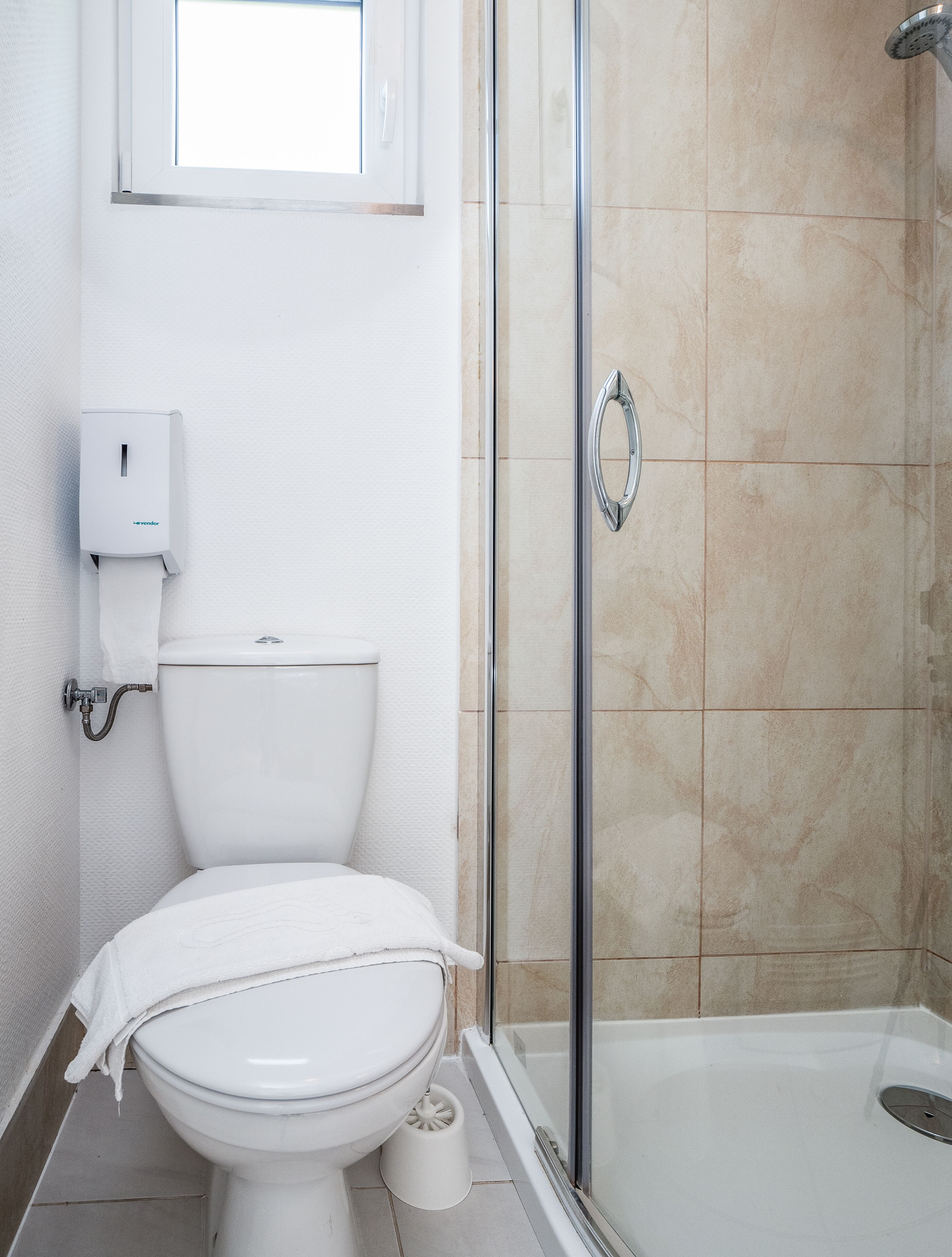 A modern bathroom with a toilet, a glass shower enclosure, and a white towel on the seat.