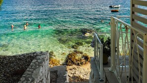 Une vue dégagée sur une zone côtière, avec un escalier menant à une plage, des bateaux sur l’eau et une côte visible au loin.