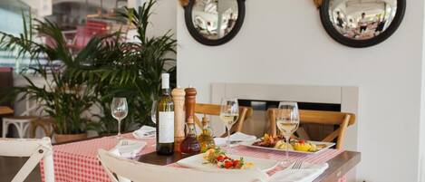 A dining table set with a checkered tablecloth, wine glasses, and bottles, surrounded by white chairs.