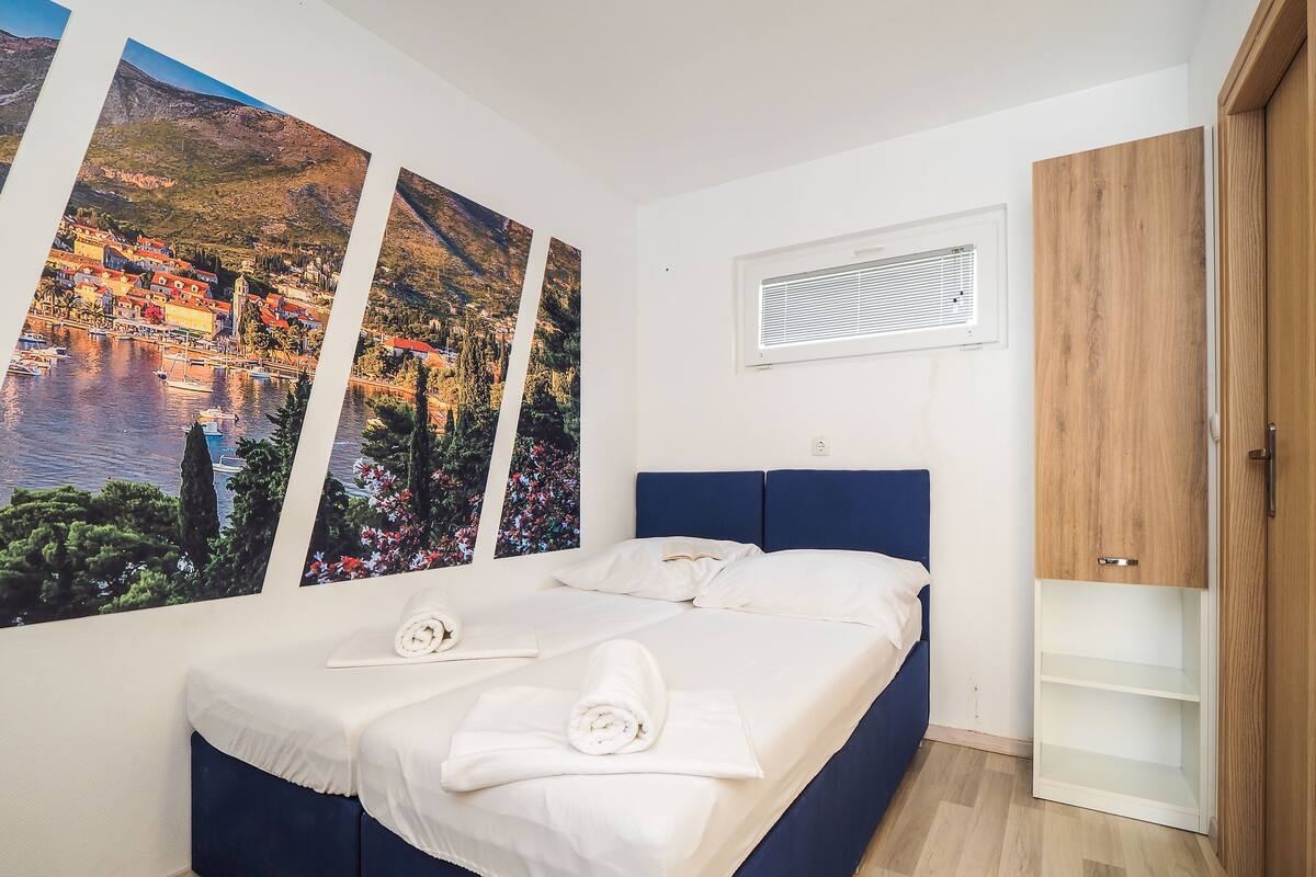 A bedroom with a bed, a wardrobe, and three large landscape paintings on the wall.