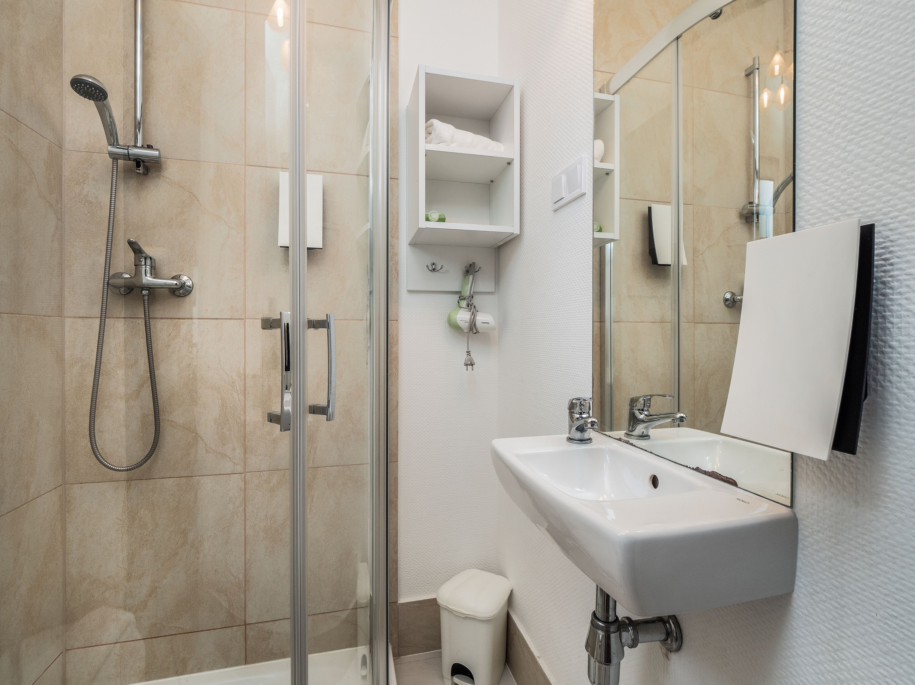 A modern bathroom with a glass shower enclosure, a white sink, and a large mirror.