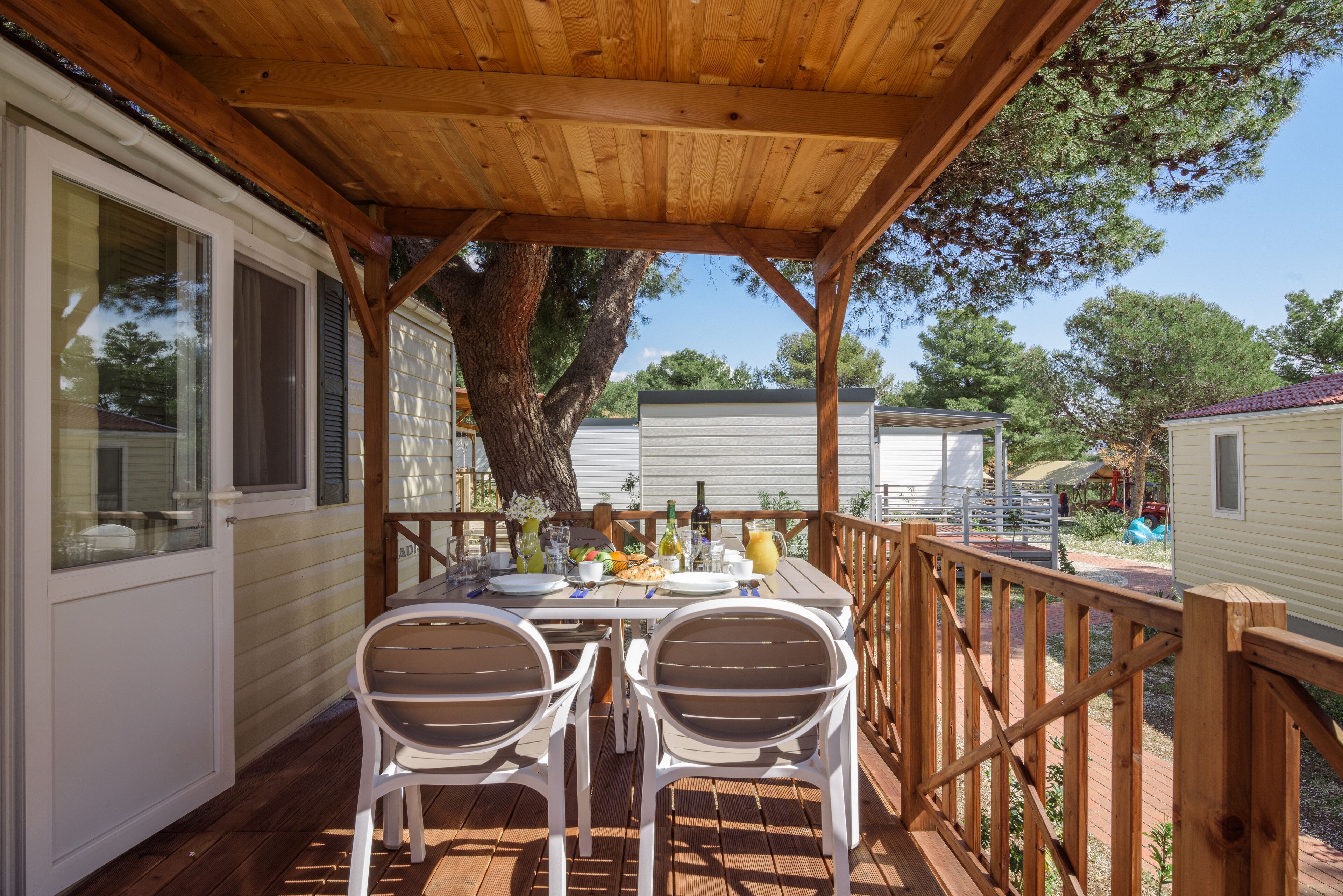 Un área de comedor al aire libre techada con cubierta de madera, sillas blancas y una mesa dispuesta para dos.