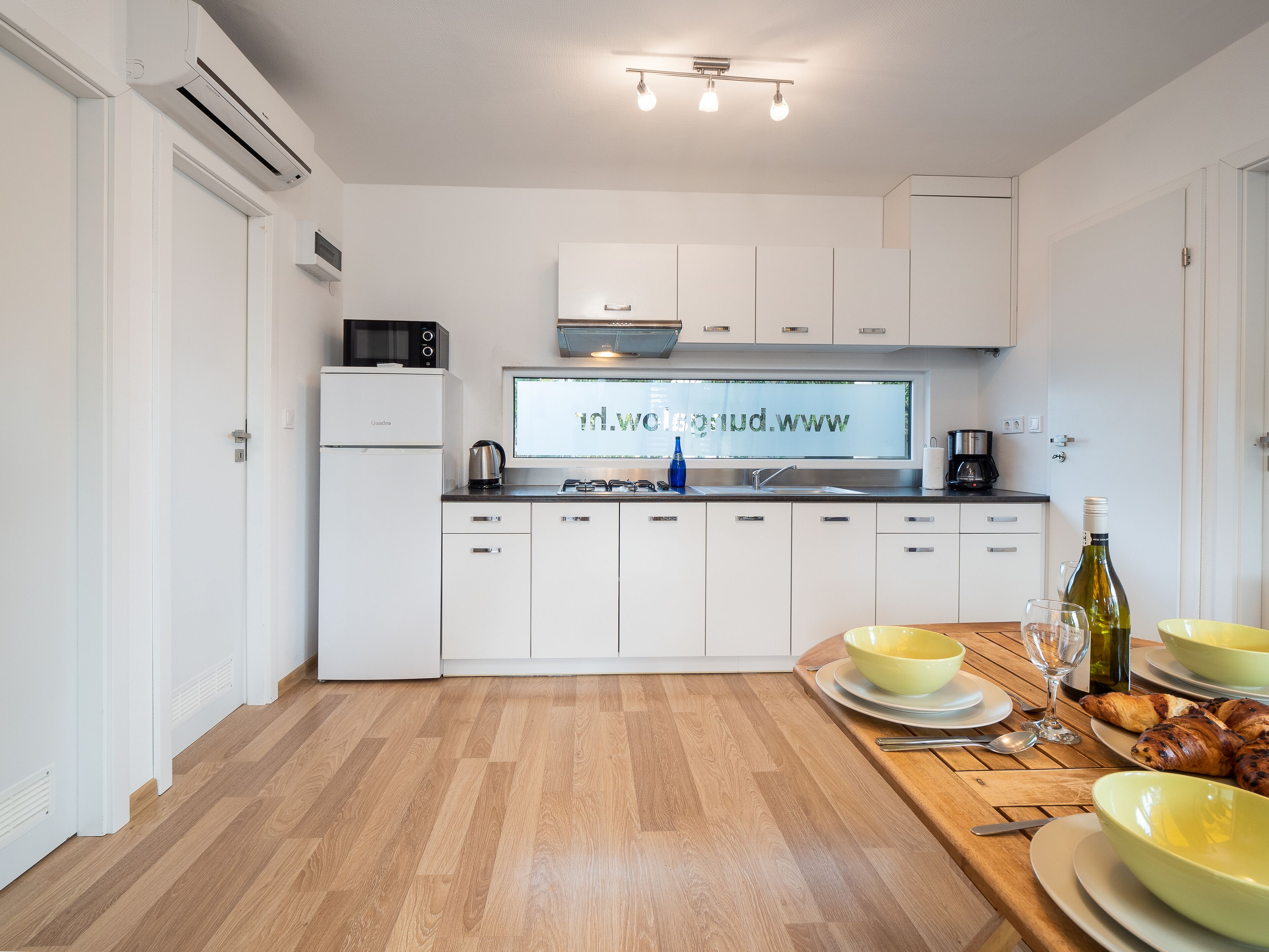 A modern kitchen with white cabinets, a built-in microwave, a coffee maker, and a large window displaying a website.