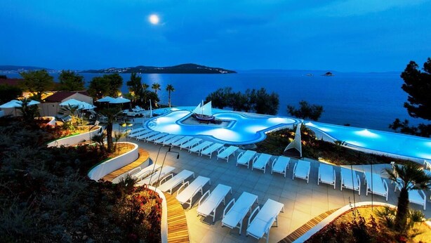 Un complexe hôtelier doté d’une piscine, de chaises longues et offrant une vue sur la mer.