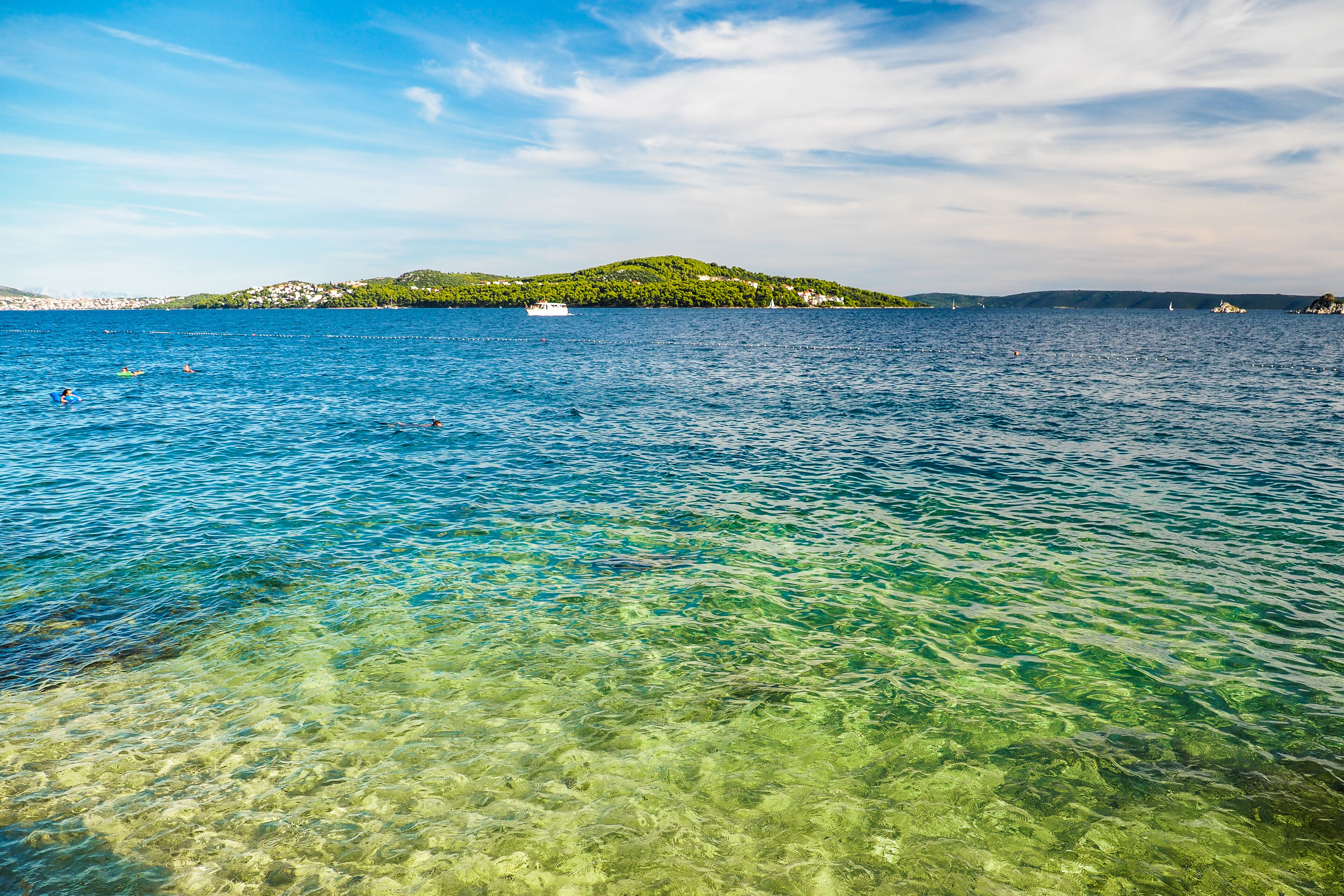 A clear view of a coastal area with a small island in the distance, calm water, and a boat.