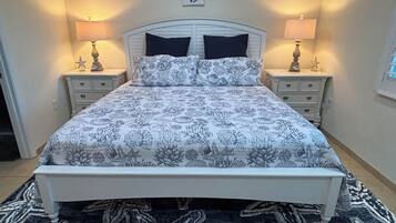 Un lit bien fait, recouvert d’une couvre-lit à motifs floraux, flanqué de deux tables de chevet avec des lampes, dans une pièce au design simple et épuré.