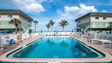 Una piscina con sillones de descanso y palmeras, rodeada de edificios con balcones.