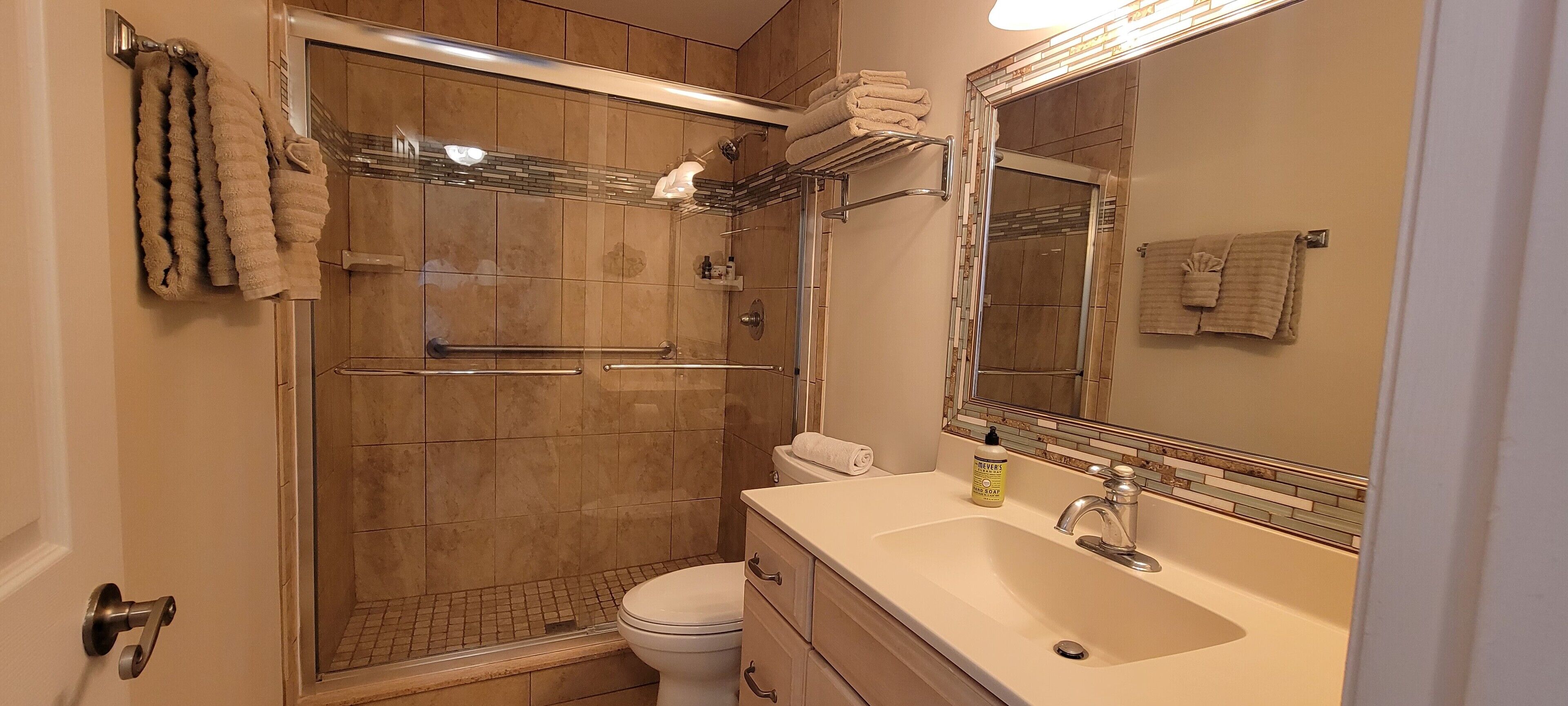 Een badkamer met een douchecabine, een wit toilet, een wastafel met spiegel en handdoeken op een rek.
