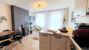 Een moderne keuken met een ingebouwde kookplaat, een eethoek met een houten tafel en zwarte stoelen, en een zithoek met een bank en een potplant.