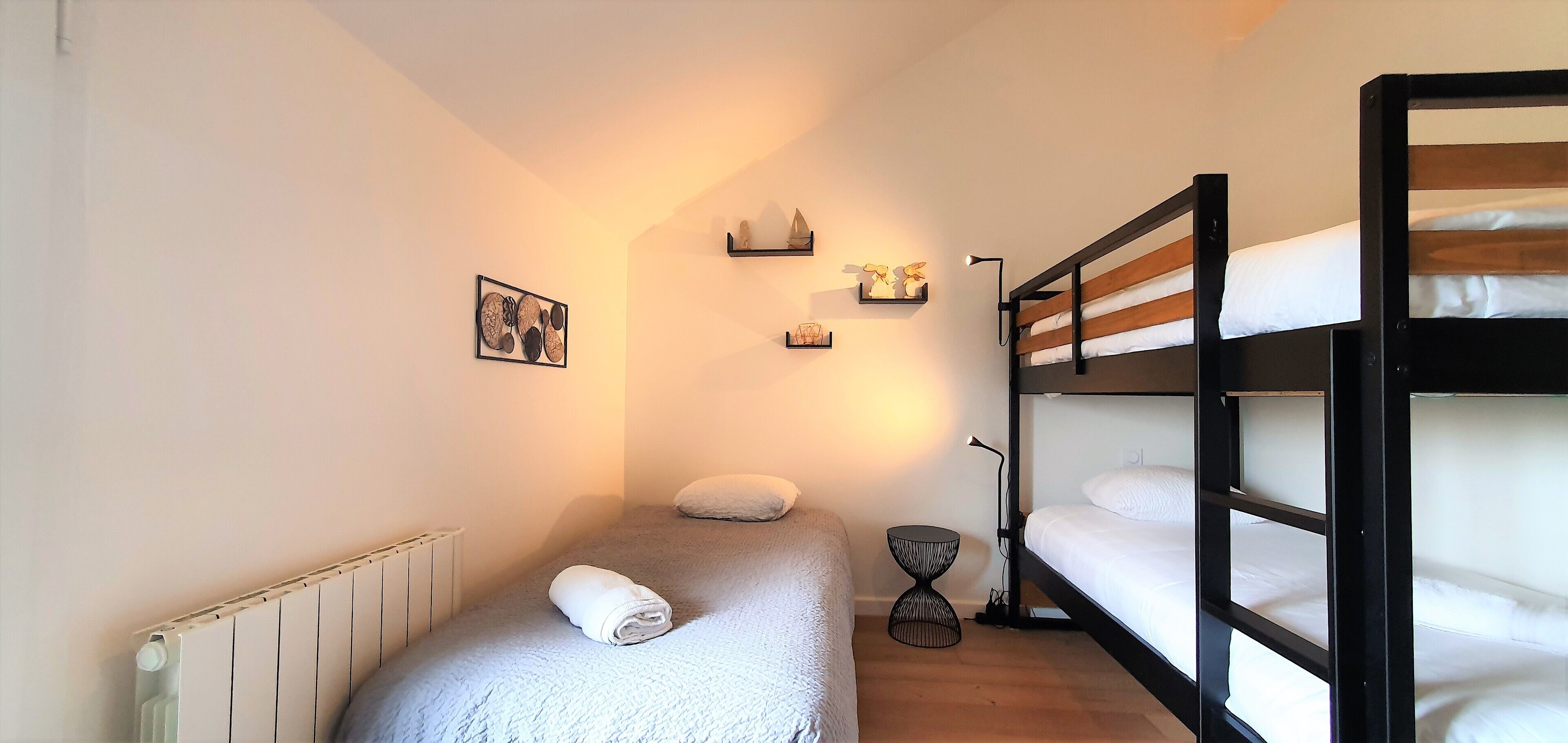 Ein kleines Zimmer mit Etagenbett, einem Einzelbett, einem Heizkörper und einem kleinen Tisch.