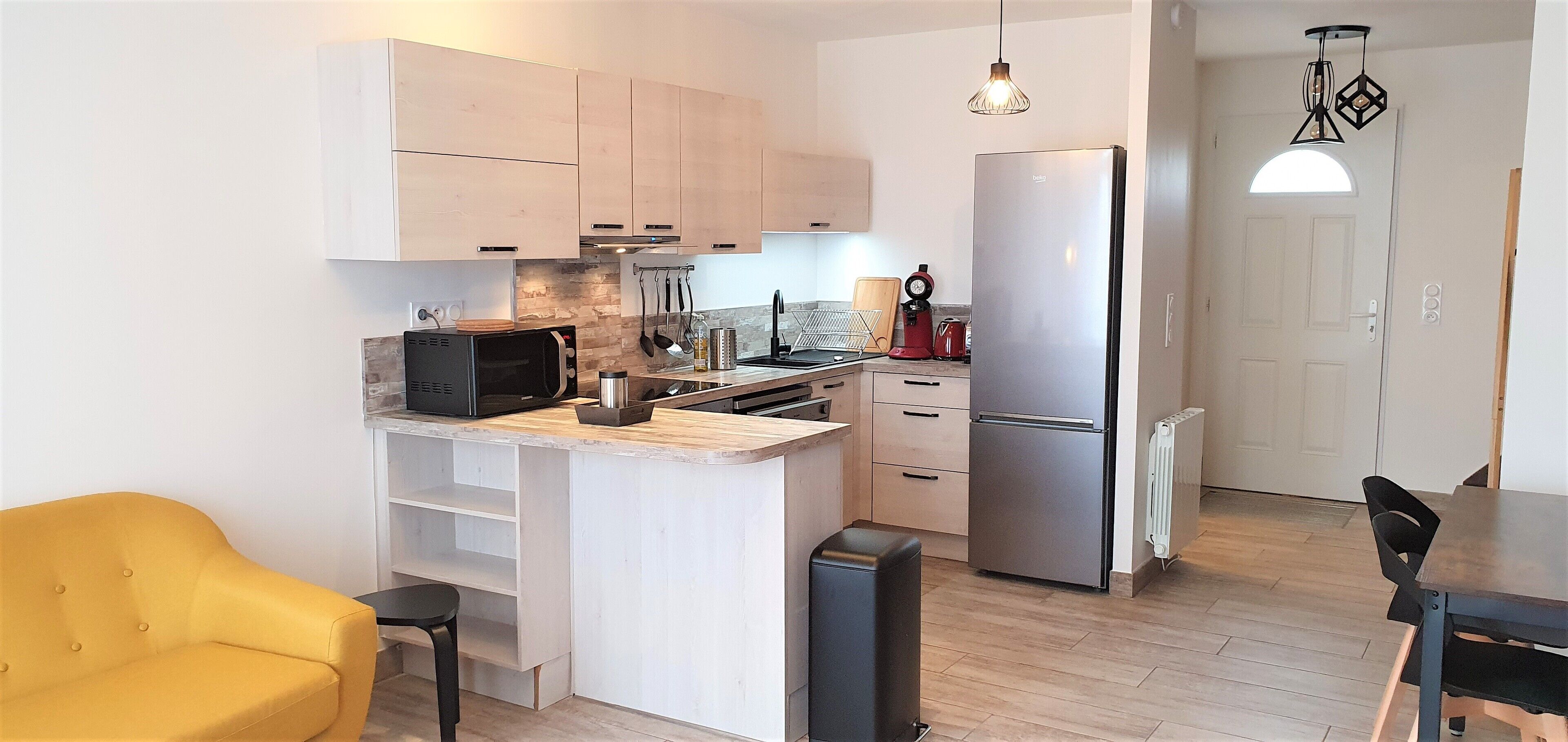 A modern kitchen with a built-in microwave, stove, and refrigerator. There is a yellow chair and a dining table with chairs.