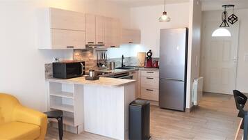 A modern kitchen with a built-in microwave, stove, and refrigerator. There is a yellow chair and a dining table with chairs.