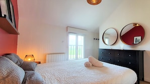 Een slaapkamer met een bed, een dressoir, twee spiegelwanden en een raam met uitzicht op groen.
