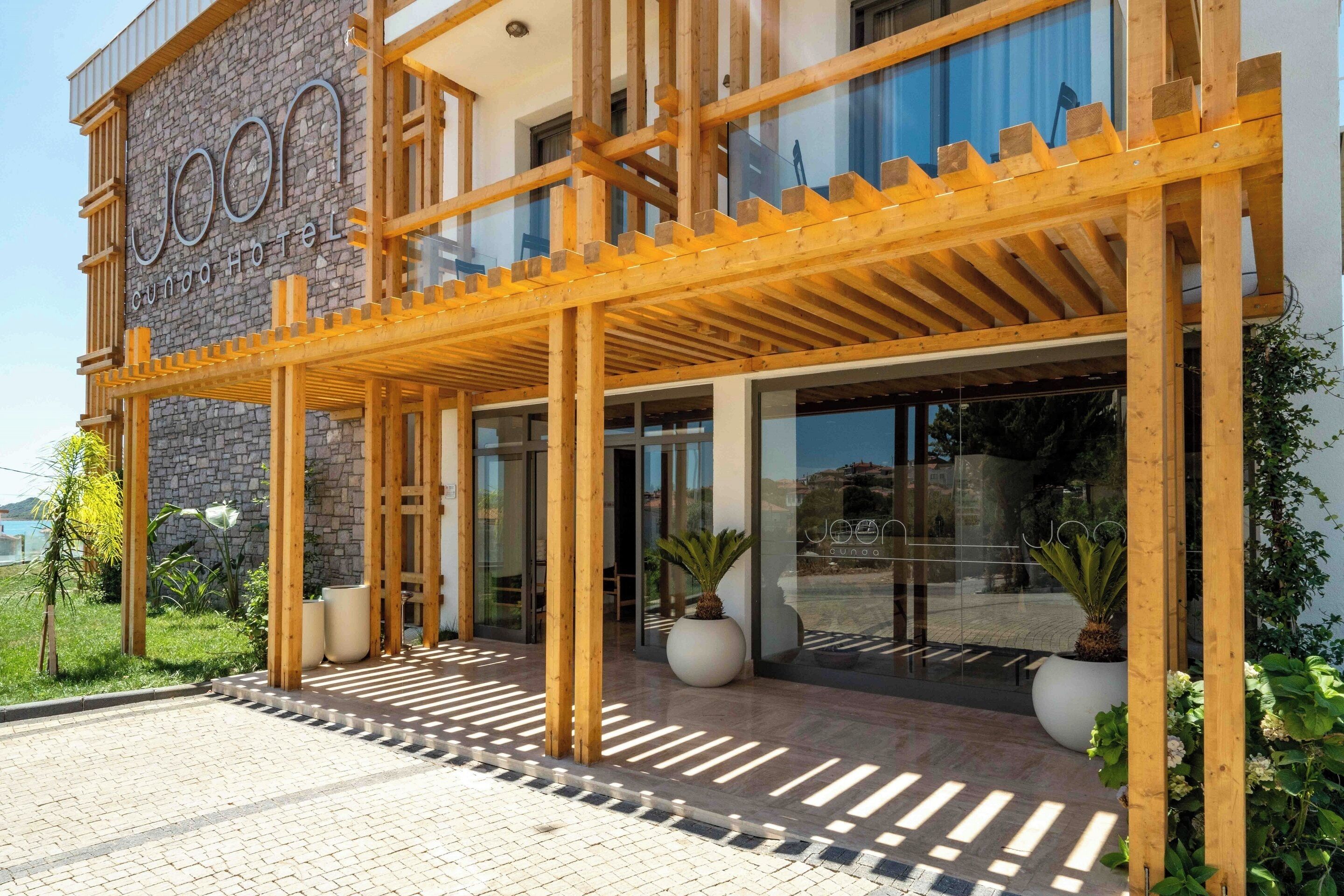 A hotel entrance with a wooden pergola, stone facade, and potted plants.
