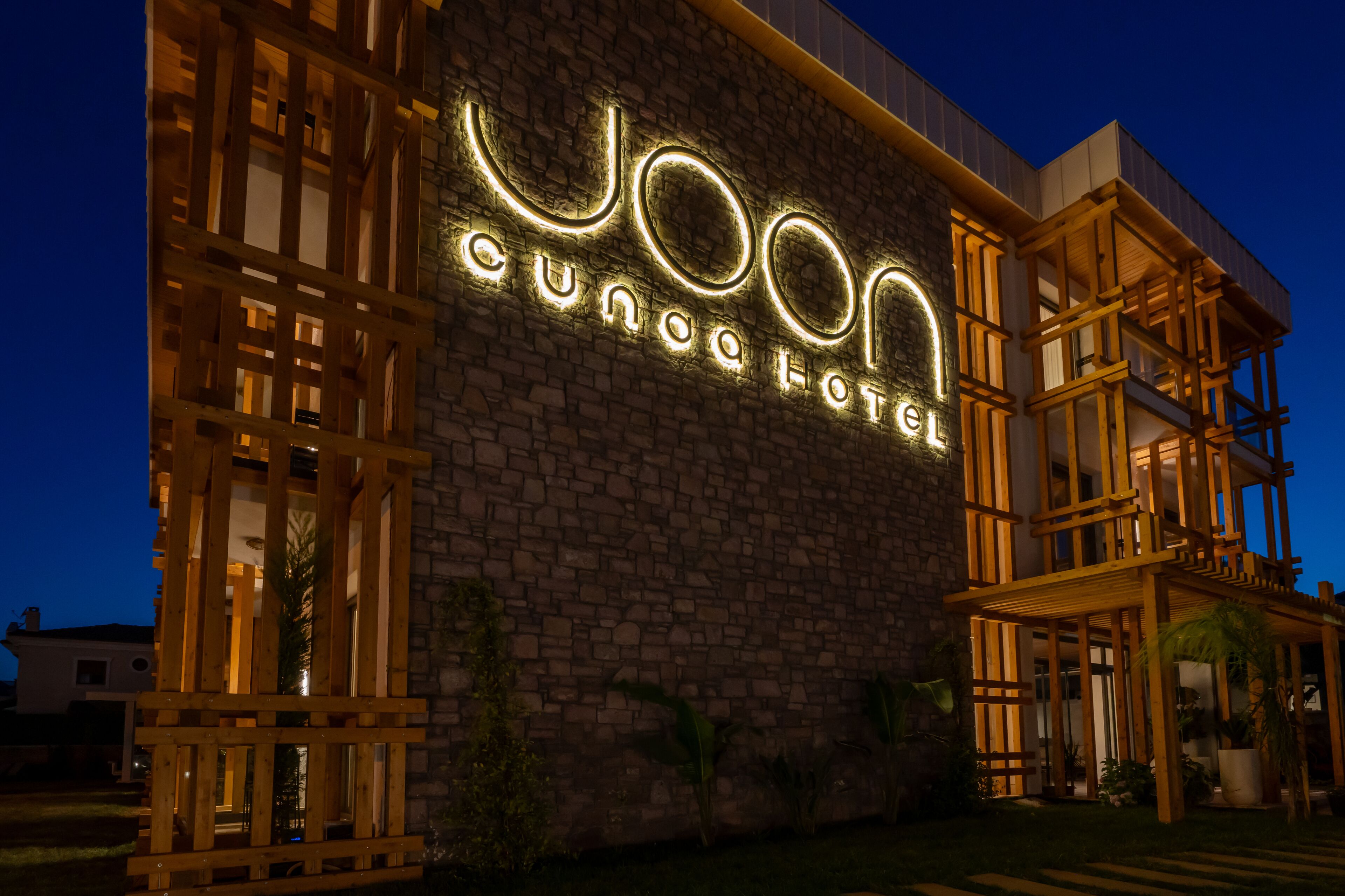 Exterior del Hotel Yoon Cuna con un llamativo letrero iluminado, fachada de ladrillo y balcones de madera.