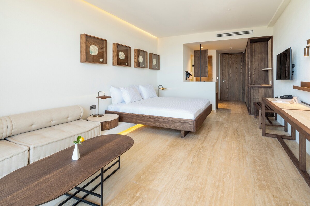 A modern hotel room with a large bed, a sofa, a wooden coffee table, and a desk.