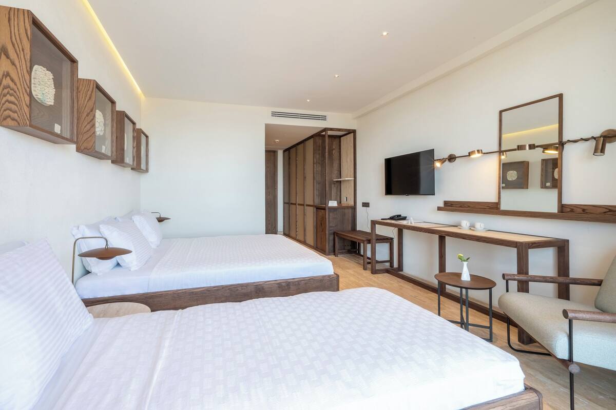 A modern hotel room with two beds, a desk, a chair, a TV, and a mirror.
