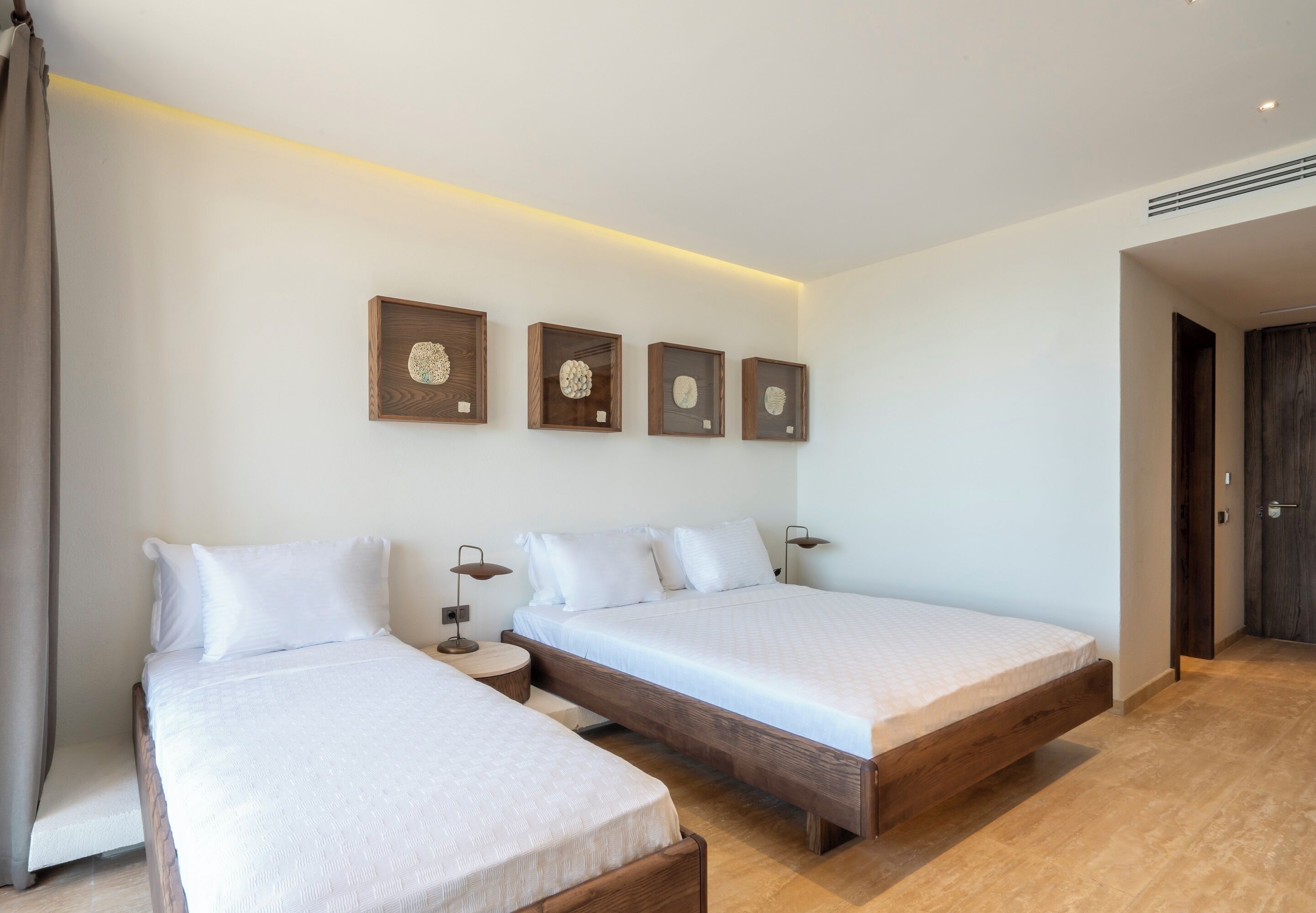 A modern hotel room with two single beds, a wooden headboard, a bedside table with a lamp, and a wall-mounted clock.