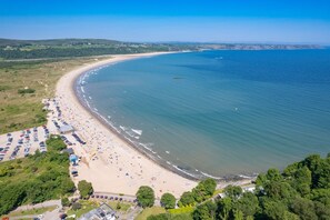 An aerial view of a coastal beach with a parking area, beach umbrellas, and a clear view of the sea. - Teacher's Cottage - Luxury Cottages (Swansea)