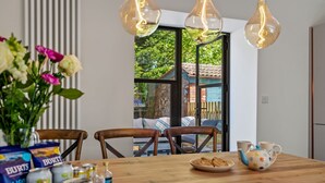 Een eetruimte met een houten tafel, stoelen, een vaas met bloemen en een raam met uitzicht op groen.