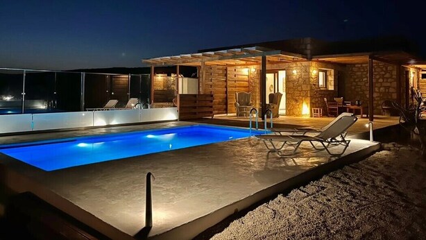 Een modern zwembad met helderblauw water, ligbedden en een stenen gebouw met een overdekt terras.